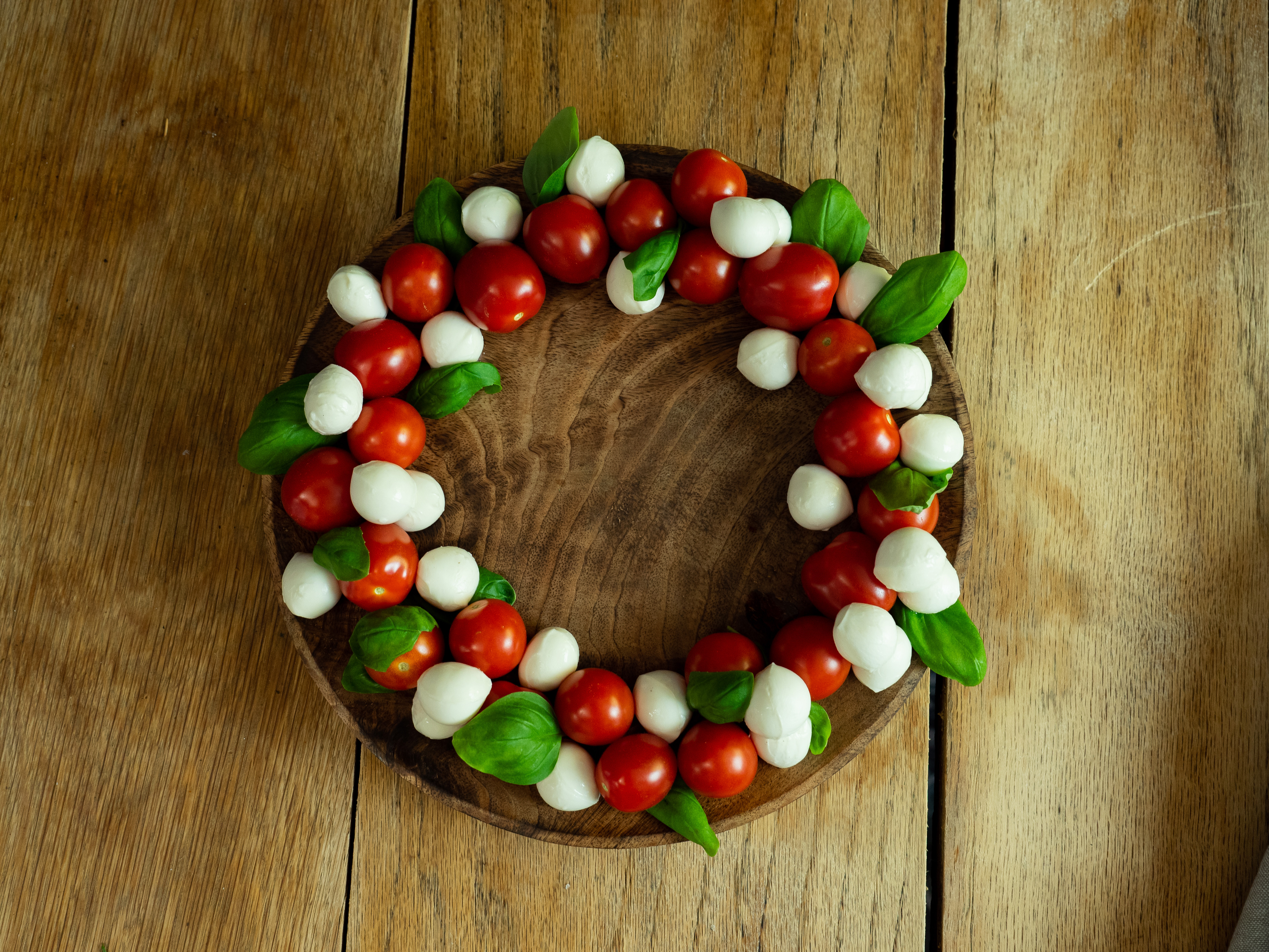 Hvite mozerella baller, røde cherrytomater og grønn basilikum ligger lagvis og i en sirkel. 